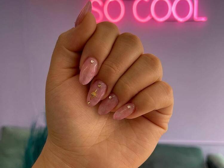 Manos mostrando diseño de uñas acrílicas con pedrería